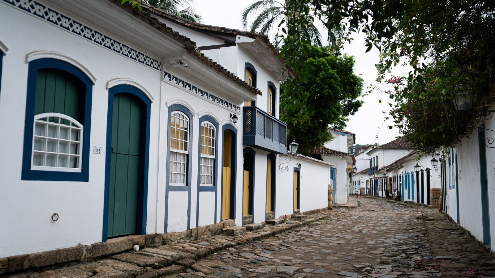 Rua de pedra no centro histórico de Paraty, no Brasil, com casas coloniais de arquitectura portuguesa, paredes brancas e portas e janelas azuis, verdes e amarelas. Imagem ilustrativa, não é um imóvel analisado pela Rivesta.