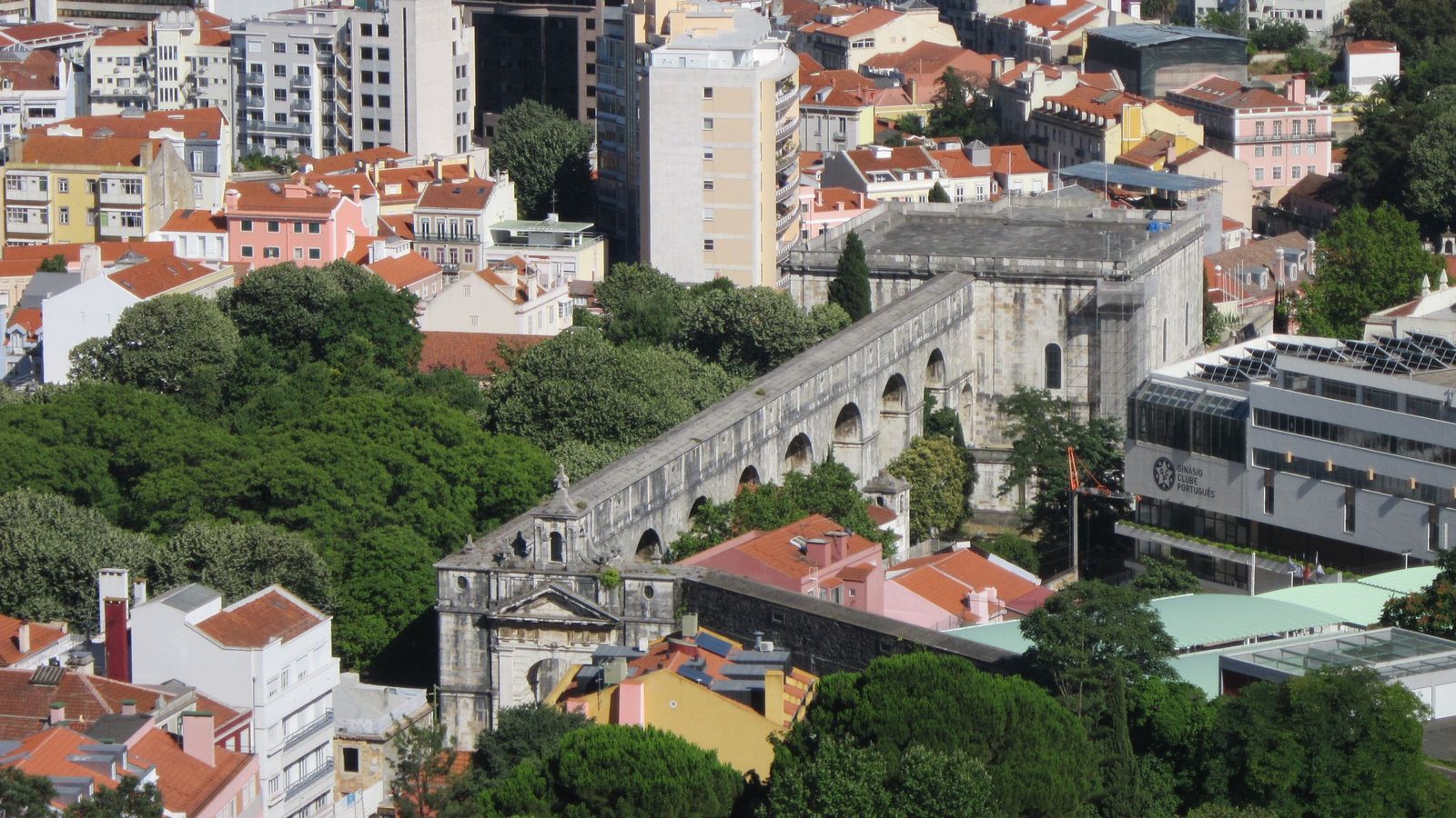 Vista aérea de Lisboa com o Aqueduto das Águas Livres a atravessar um bairro de prédios de habitação de telhados cor de laranja, entre árvores. Imagem ilustrativa, não é um imóvel analisado pela Rivesta.